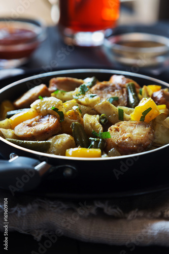 Fried potatoes with sausages in skillet