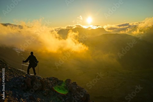 A Person Standing on the Mountain with Clouds During Sunset Sunrise