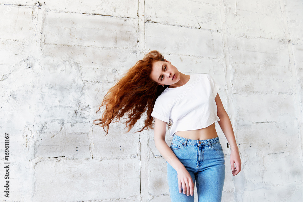 Model tests.Beautiful redhead girl with curly hair. Natural color. Dancing and moving on the background of light brick wall. Dynamics Model tests.Beautiful redhead girl with curly hair. Natural color. Dancing and moving on the background of light brick wall. Dynamics