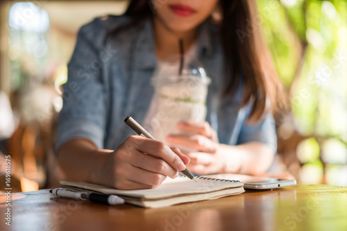 Young asian woman drinking coffee while writing on notebook. photo