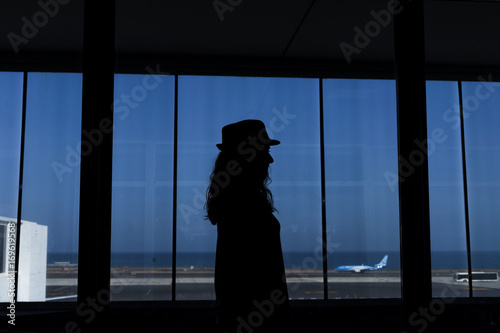 silhouette of a young woman watching an airplane taking off in the airport through a window. Travel concept.