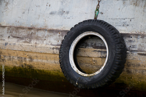 Old tire hanging from wooden boat side.