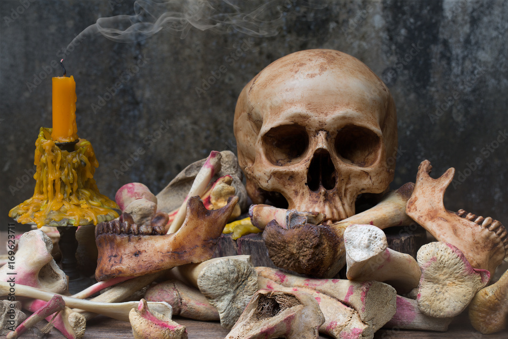 Skull with pile of bone and candle with smoke on the old wooden plate and old dirty wall in Halloween night