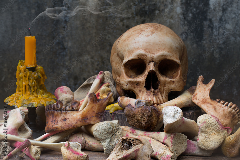 Skull with pile of bone and candle with smoke on the old wooden plate and old dirty wall in Halloween night Skull with pile of bone and candle with smoke on the old wooden plate and old dirty wall in Halloween night