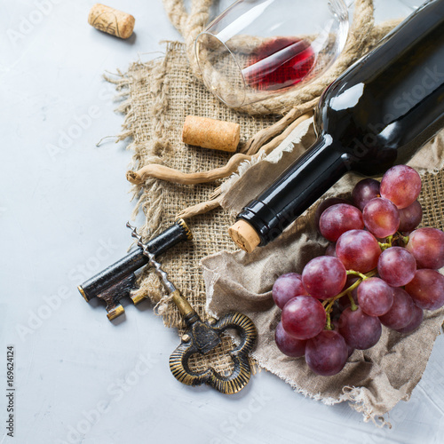 Bottle, corkscrew, glass of red wine, grapes on a table