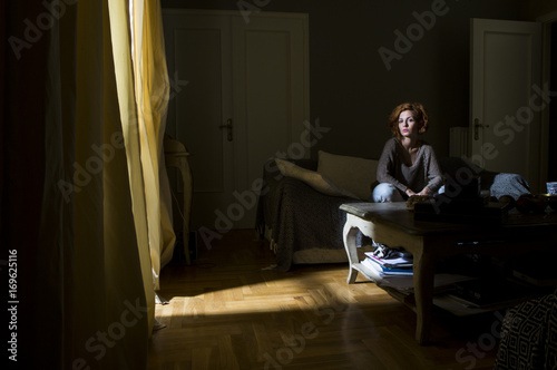 A young beautiful woman sitting on a sofa in a dark room photo