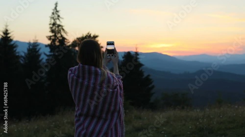 Woman girl holding smart phone taking photo picture standing back view sunset background fiery colored sky photograph landscape rest enjoying nature vacation summer evening memory wrapped blanket dusk photo