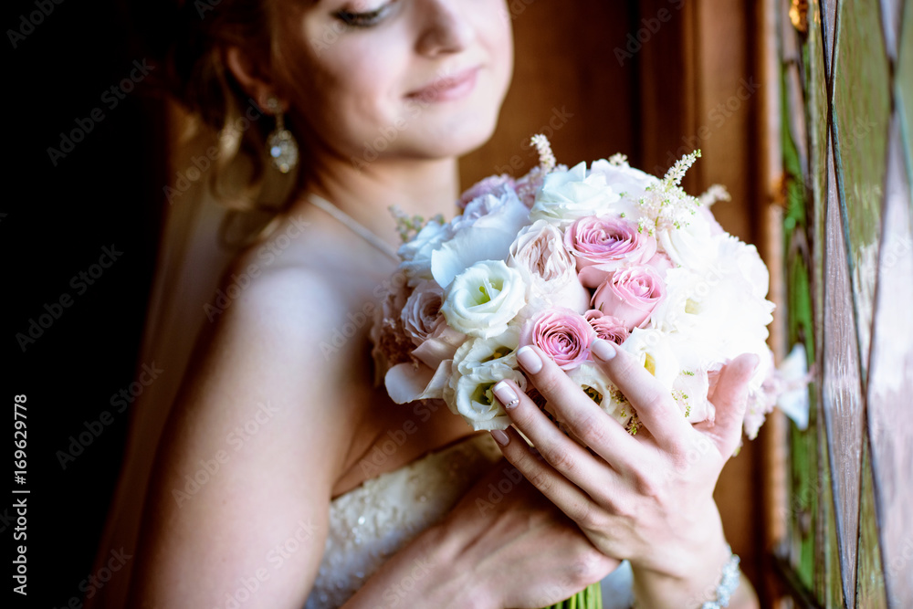 Naklejka premium Beauty bride in bridal gown with bouquet and lace veil indoors