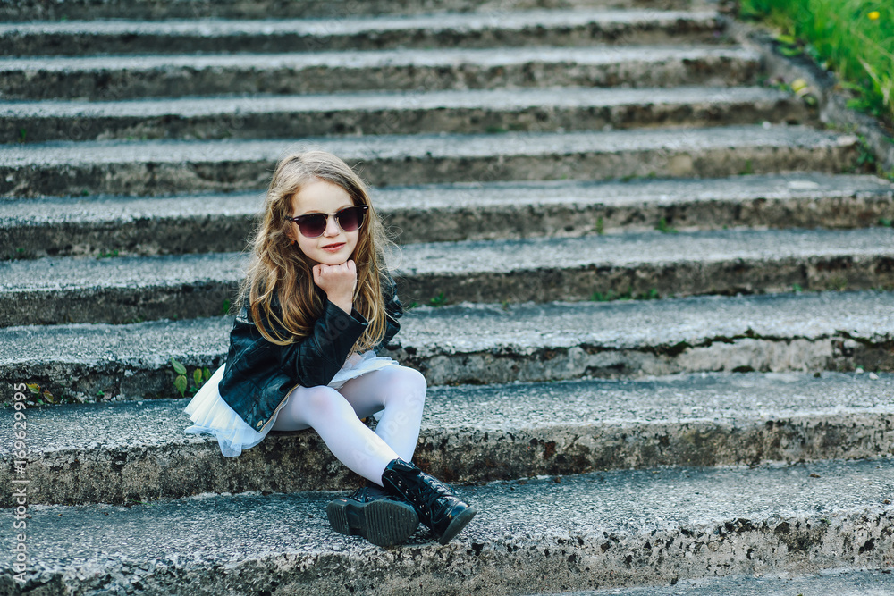 Obraz premium Up view of a happy little girl on the steps pointing at a camera