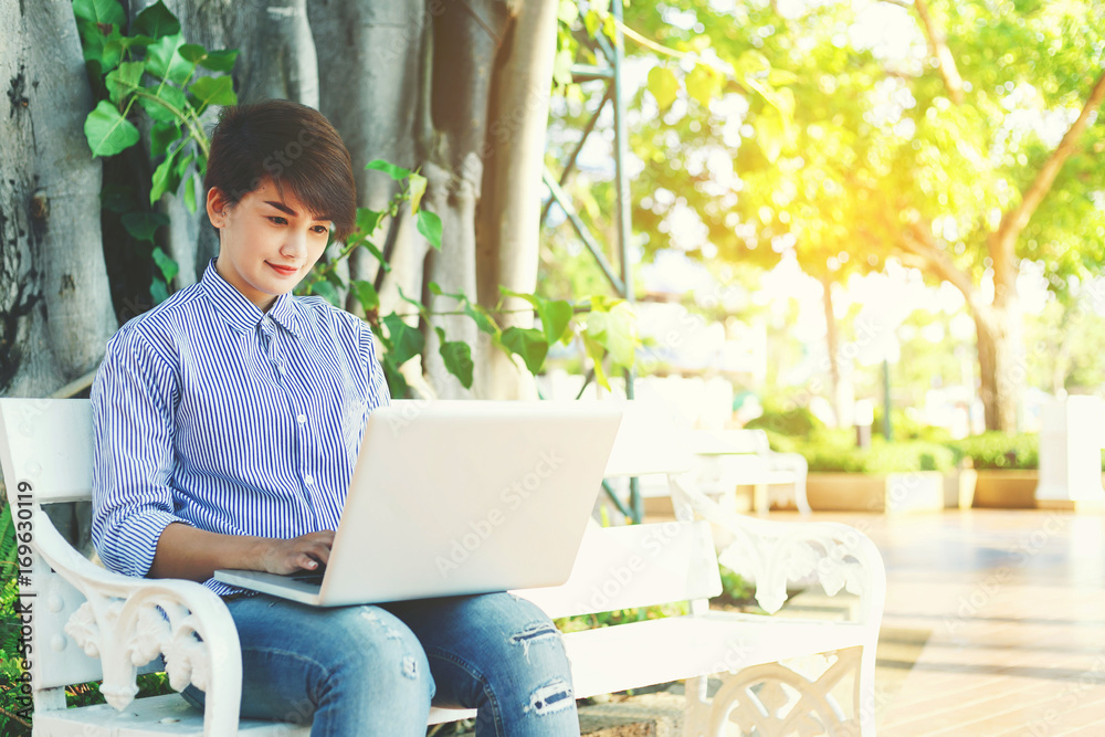 Beautiful short hair woman sitting on white chair under the tree and typing laptop for outdoor working working her business in the park. Beautiful short hair woman sitting on white chair under the tree and typing laptop for outdoor working working her business in the park.