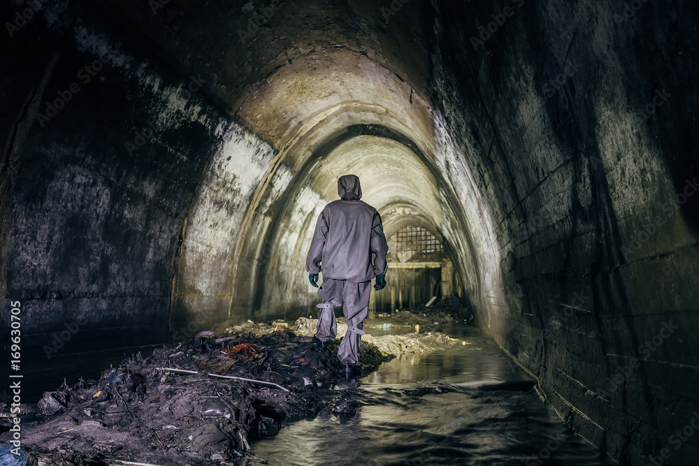Sewer tunnel worker in chemical protective suite in underground gassy sewer tunnel  - obrazy, fototapety, plakaty 