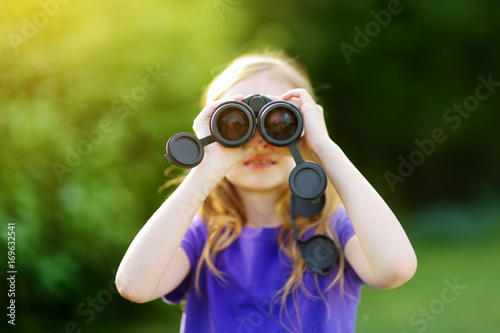 Funny little girl looking through binoculars on sunny summer day