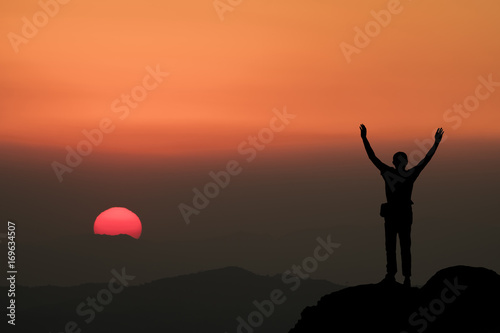 Silhouette of man hold up hands on the peak of mountain