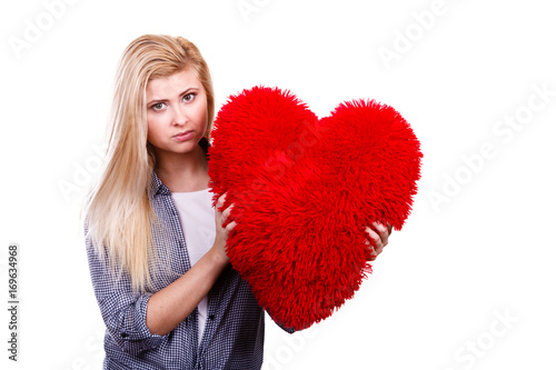 Sad girl holding big red pillow in heart shape