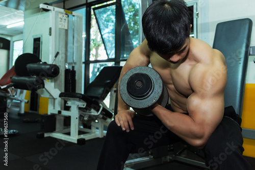 Fitness man in training showing exercises with dumbbells in gym