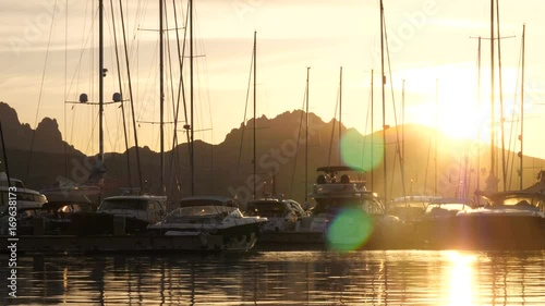 Backlit view of power and sailing boats docked at the sunset in Porto Rotondo, Italy.