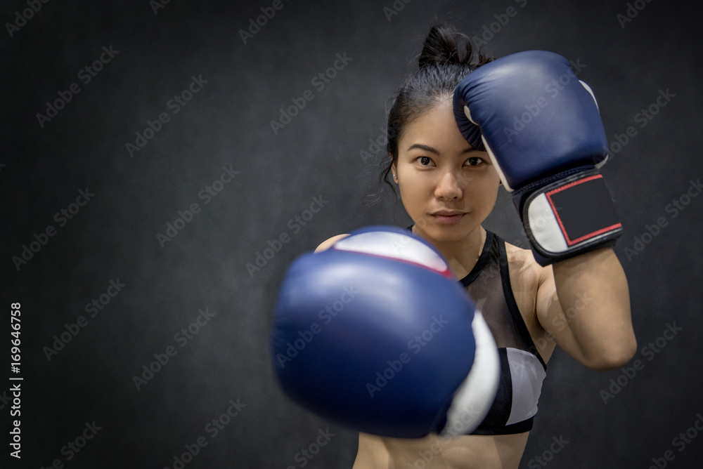 Attractive young Asian woman posing with blue boxing gloves on black background