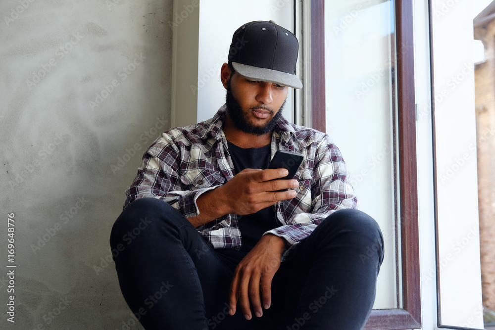 A black male sits near window and using a smartphone.