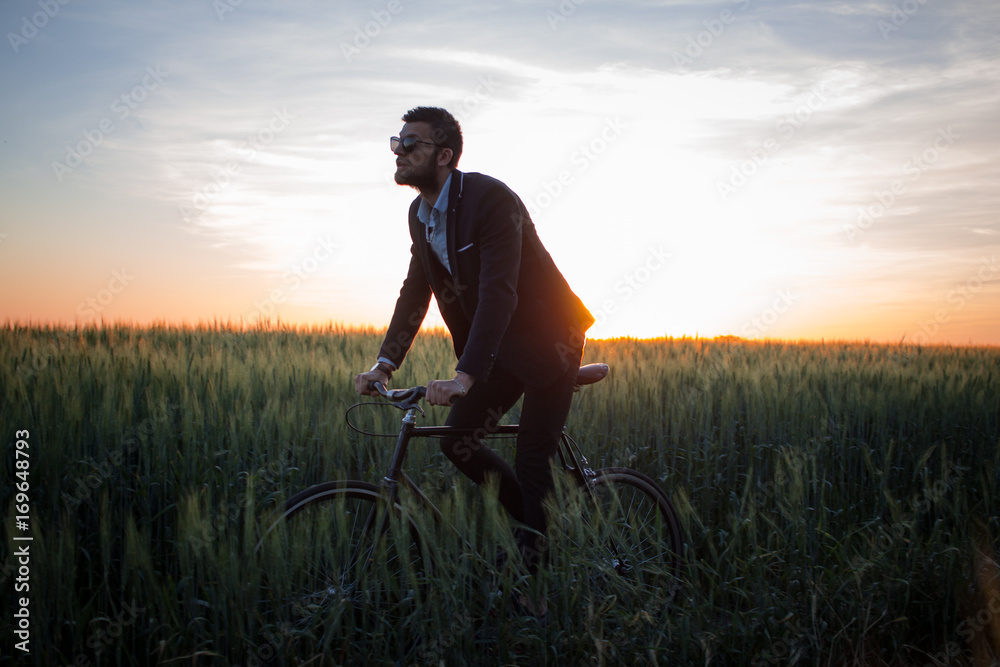 Fototapeta premium A caucasian businessman riding a bicycle in summer fields, Male in business suit ride on fixie bike.