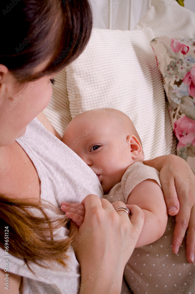 Breastfeeding baby. Young mother holding her newborn child. Mom nursing baby. Woman and new born boy in white bedroom.