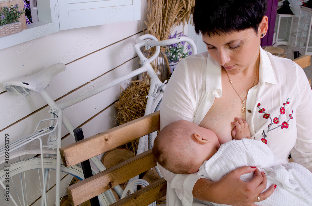 Breastfeeding baby. Young mother holding her newborn child. Mom nursing baby. Woman and new born boy in white bedroom.