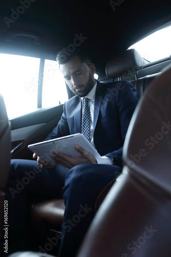 businessman with a digital tablet sitting in the back seat of a  © ASDF