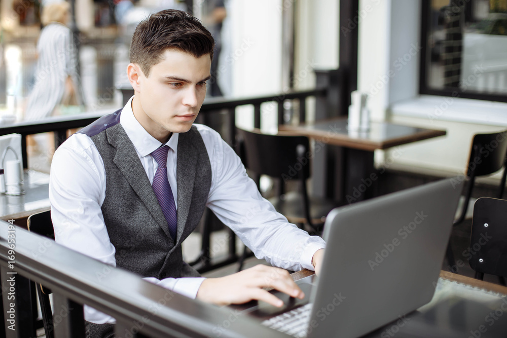 Successful young businessman typing on laptop in cafe