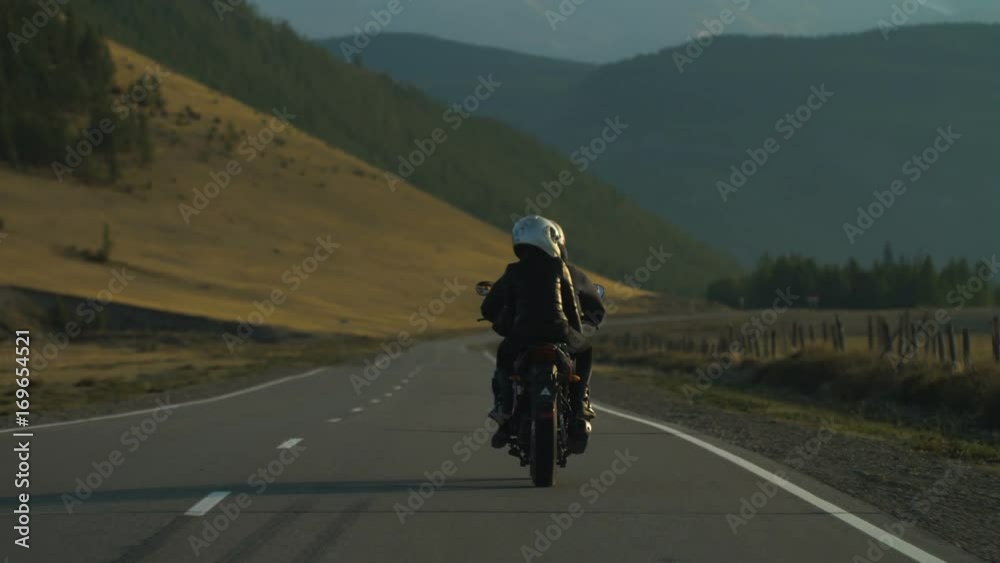 Couple of Motorcyclists on a Motorcycle are Driving along a Beautiful Country Road Couple of Motorcyclists on a Motorcycle are Driving along a Beautiful Country Road
