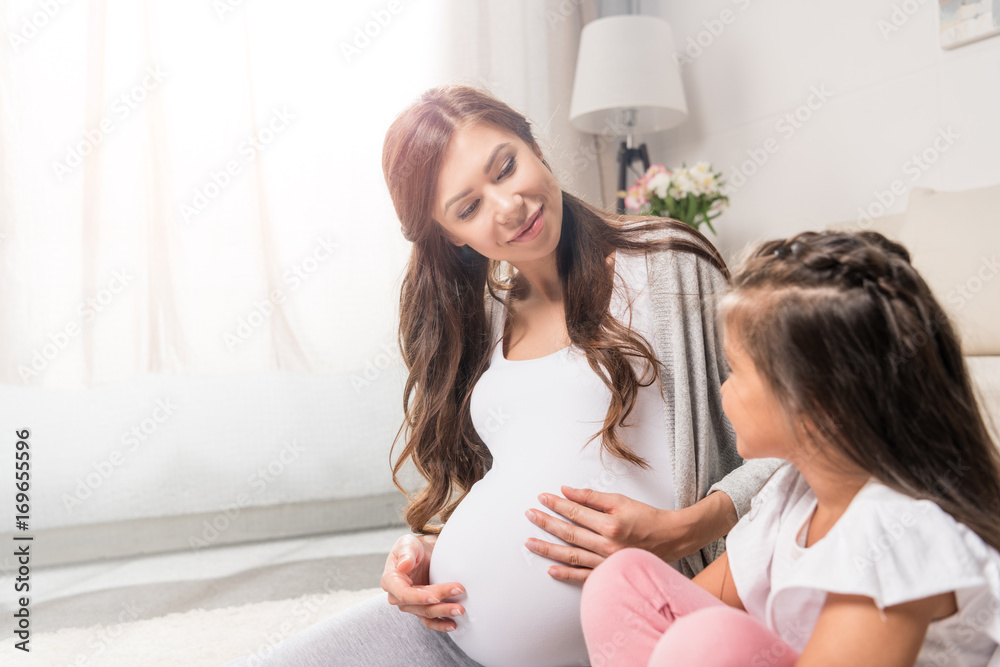 Pregnant woman with daughter sitting on rug Pregnant woman with daughter sitting on rug