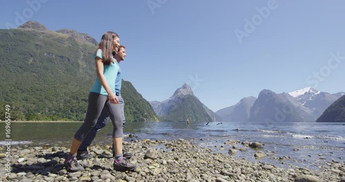 Tourists hiking in New Zealand in Milford Sound by Mitre Peak in Fiordland. Couple on New Zealand travel visiting famous tourist destination and attraction on south island, New Zealand. photo