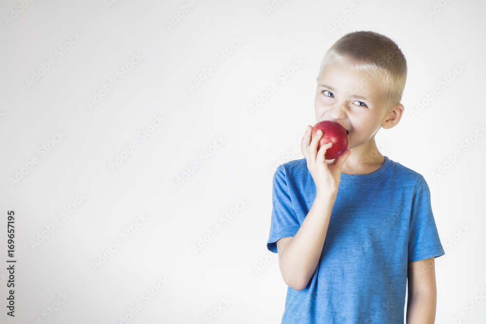 Portrait happy, smiling boy eats an red apple. Funny child holding an apple. Looking at camera. The concept of a healthy lifestyle, organic vegetarian food. Portrait happy, smiling boy eats an red apple. Funny child holding an apple. Looking at camera. The concept of a healthy lifestyle, organic vegetarian food.