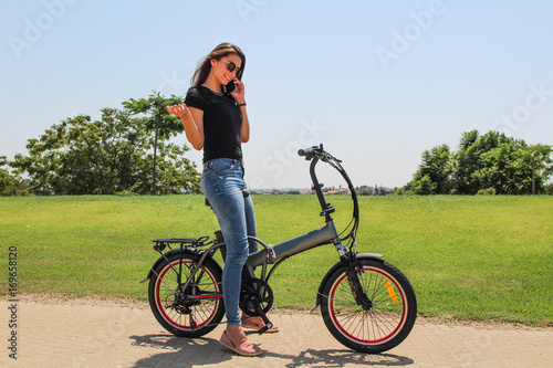 A smiling woman with an electric e bike talking on the phone in the park