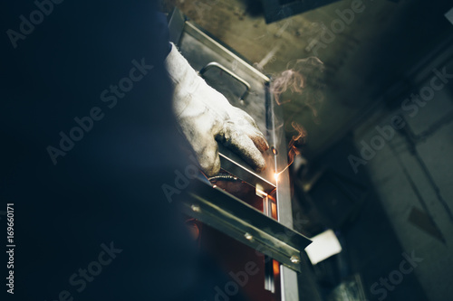 Metallurgy industry. Factory for production of heavy pellet stoves and boilers. Close up of manual worker welder on his job. Extremely dark conditions and visible noise.