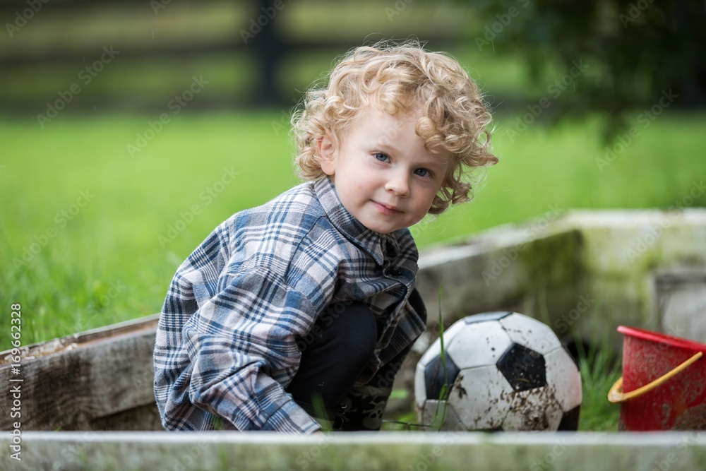Young caucasianboy with curly hair playing in sandbox Young caucasianboy with curly hair playing in sandbox