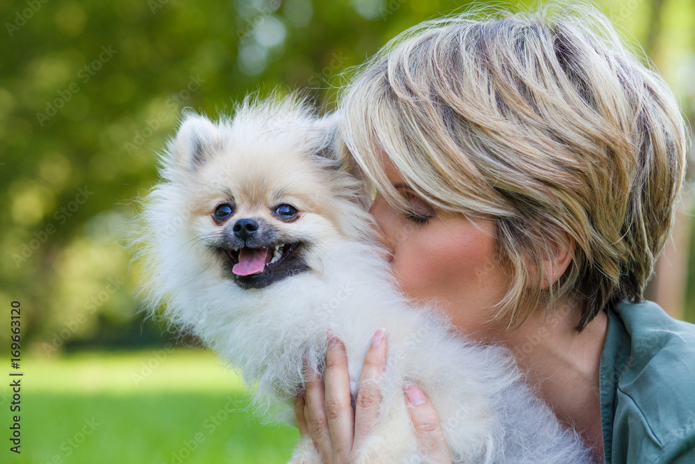 Frau küsst kuscheliges Fell eines glücklichen Zwergspitz Hundes