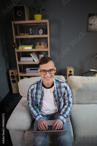 Portrait of young freelancer man sitting on sofa working on laptop. Home office concept, male staying at home working on project.