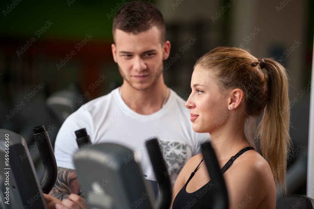 Fototapeta premium Personal trainer helping his female client in gym