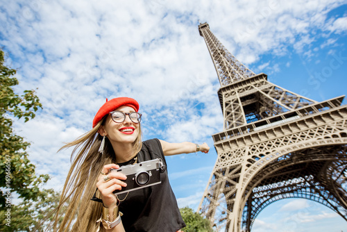 Portrait of a young happy woman tourist in red cap with photo camera in front of the Eiffel tower in Paris © rh2010
