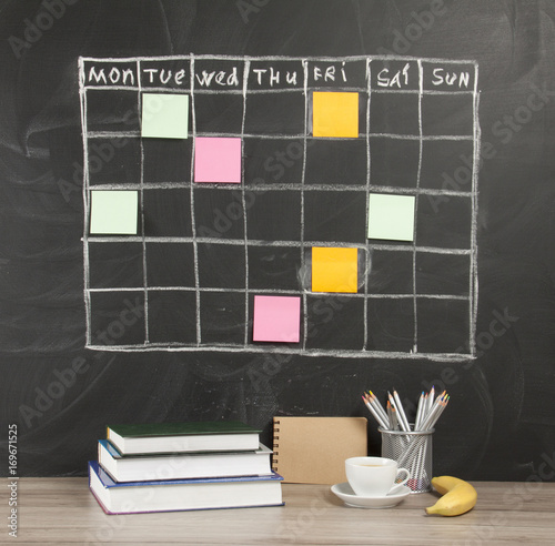 Grid timetable schedule with note paper on black chalkboard background. photo