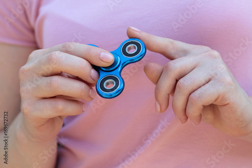 girl playing blue metal spinner in hands on the street, female hands holding popular fidget spinner toy on gray background, anxiety relief toy, anti stress and relaxation fidgets. photo