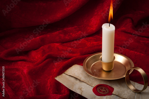 Masonic secrecy concept with a lit candle on a letter made of old vintage paper with red wax seal stamp and the freemason emblem against a scarlet color velvet background with copy space photo