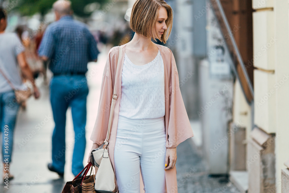Beautiful and fashionable young woman with shopping bags standing on city street and looking at shopfront Beautiful and fashionable young woman with shopping bags standing on city street and looking at shopfront