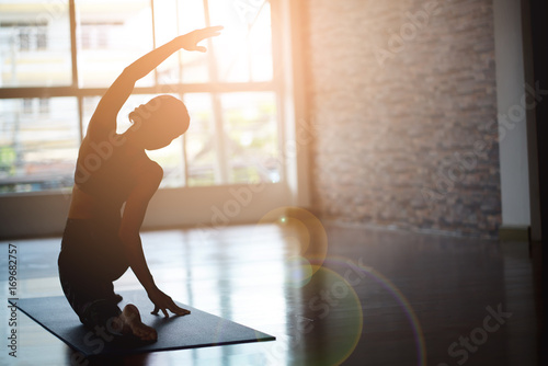 Asian woman doing yoga in a room with sunlight coming through the window.