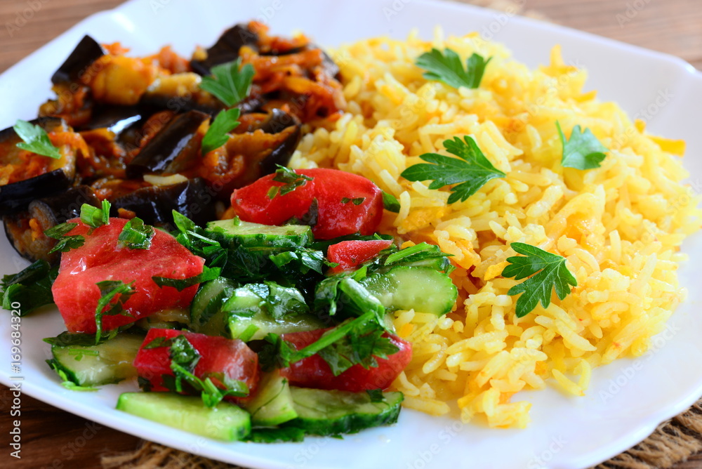 Basmati rice with stewed vegetables and fresh salad. Boiled rice basmati, stewed eggplant, tomato and cucumber salad with greens on a plate. Easy vegetarian recipe. Closeup Basmati rice with stewed vegetables and fresh salad. Boiled rice basmati, stewed eggplant, tomato and cucumber salad with greens on a plate. Easy vegetarian recipe. Closeup
