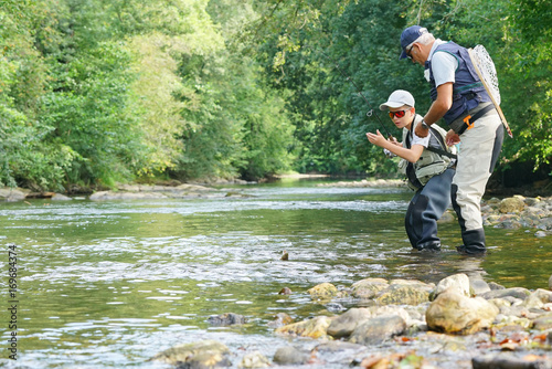 Father and son fly-fishing and catching rainbow trout in river
