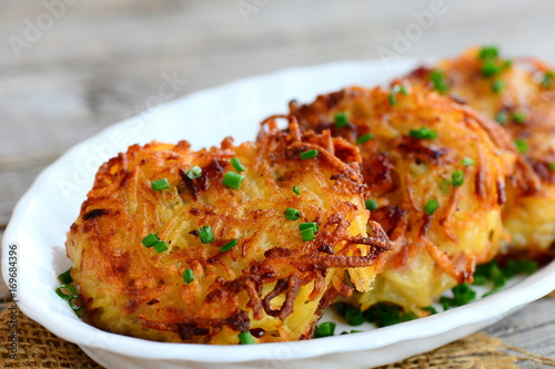 Fried potato pancakes or draniki with ham slices and green onion on a white plate. Simple draniki recipe. Closeup