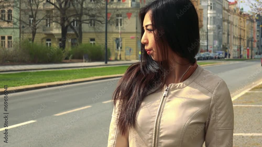 A young Asian woman waits impatiently for someone in a street in an urban area A young Asian woman waits impatiently for someone in a street in an urban area