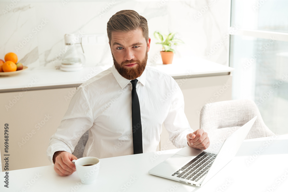 Bearded business man sitting by the table in kitchen