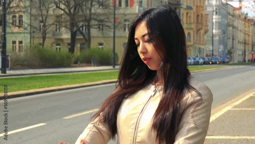 A young Asian woman adjusts her hair and clothes and poses for the camera with a smile in a street in an urban area A young Asian woman adjusts her hair and clothes and poses for the camera with a smile in a street in an urban area