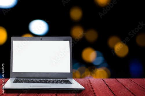 white blank screen laptop computer on wooden desk for presentation with blurred image of abstract night light circular bokeh in dark background, copy space,lifestyle lifestyle concept